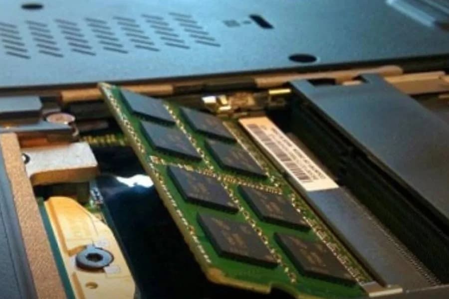 Pente de memória RAM sendo encaixado no slot de um notebook aberto.