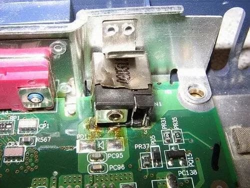 Conector de alimentação queimado na placa de um notebook, com marcas escuras em volta.