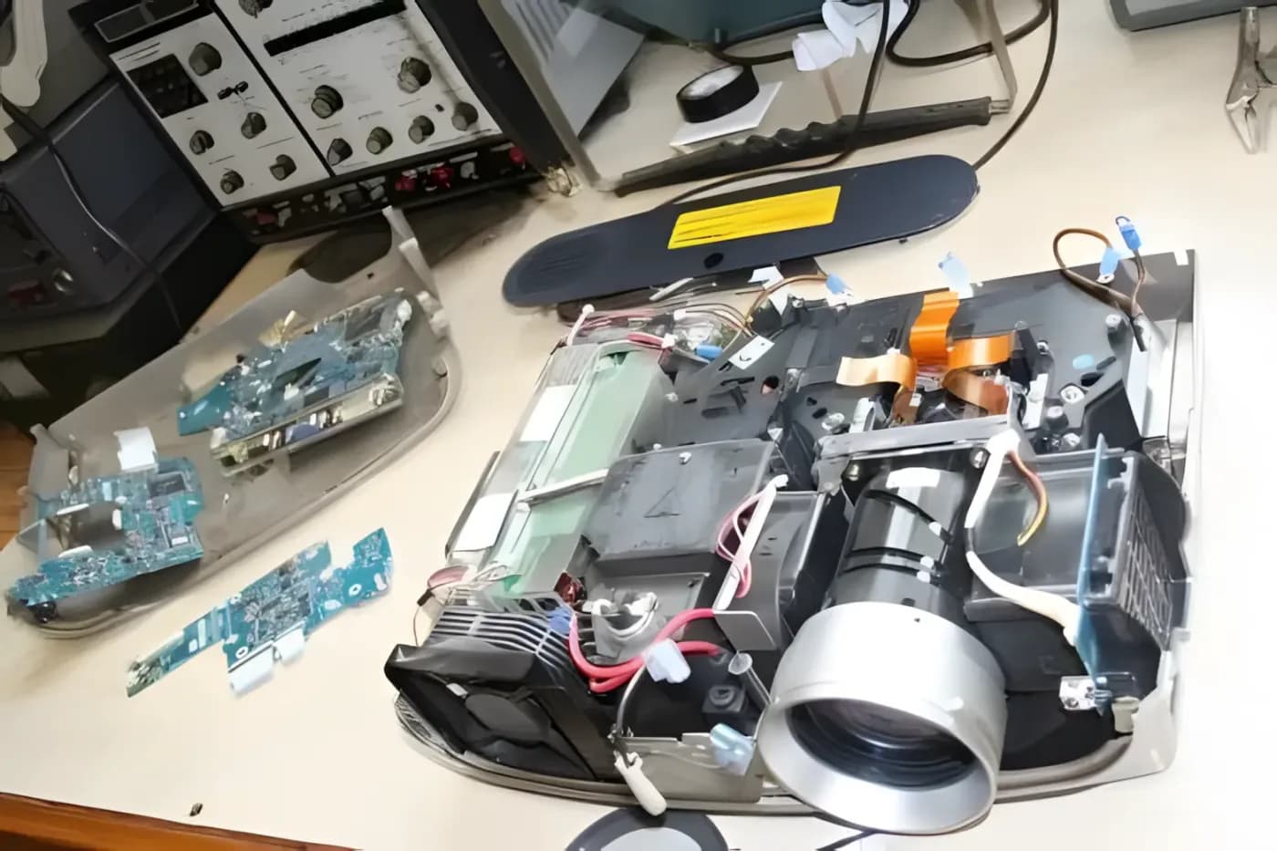 Projetor aberto na bancada, com a lente, o cooler e as placas à vista.